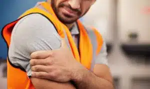 A man wearing an orange hi-vis vest holding his right shoulder in pain.