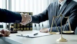 A solicitor in a grey suit sits behind a desk and shakes hands with a client